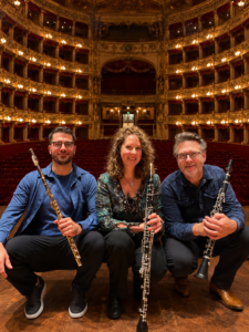 Drie muzikanten met blaasinstrumenten poseren in een historisch concertgebouw